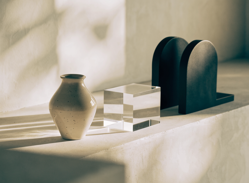 A small group of minimal home objects arranged on a plaster ledge in warm afternoon light