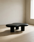 Cloud Coffee Table, black irregular top on three cylindrical legs, in a bare room with pale oak flooring