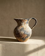 Wabi-Sabi Terracotta Vase, a pitcher form with rust and slate mottled glaze, on a plaster ledge in warm light