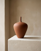 Teardrop Ceramic Vase in ribbed terracotta with a slender neck, on a plaster plinth against a warm wall
