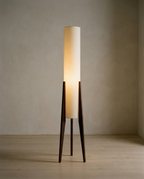 Japanese Floor Lamp, a tall cylindrical fabric shade on three tapered dark wood legs, lit in a bare room