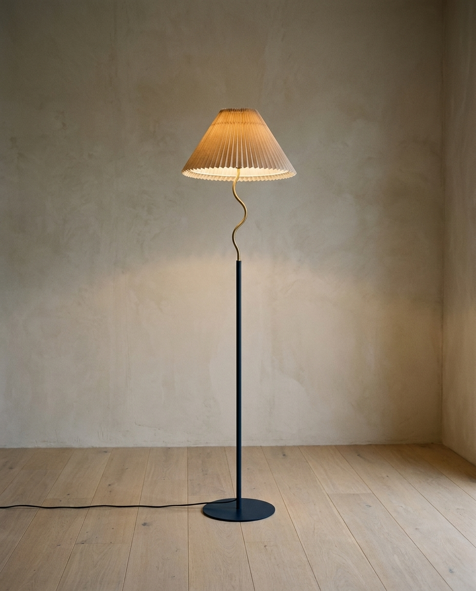 Pleated Floor Lamp with a pleated shade on a curved brass stem and slim dark pole, lit in a bare room with oak flooring