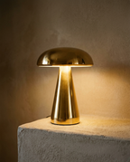 Mushroom Table Lamp with a polished brass dome on a tapered stem, glowing warm on a plaster ledge
