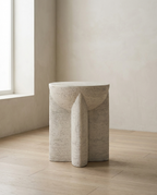 Curved Stone Side Table in textured white stone with curved cut-out legs, in a bare room with oak flooring