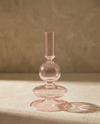 A pink glass candlestick of stacked bubble forms, casting a coloured shadow on a plaster surface