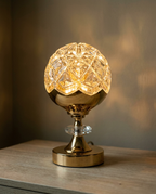 A faceted crystal globe lamp on a polished brass base, lit warm on a wooden surface
