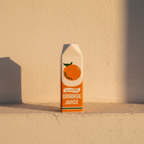 Ceramic vase modelled as an orange juice carton on a plaster ledge