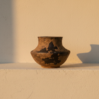 Squat speckled clay jar with dark patches where the glaze pulled away