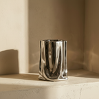 Crumpled chrome vase on a plaster ledge in golden hour light
