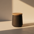 Drum side table with a dark textured stone body and warm wood top