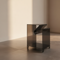 Smoked grey acrylic C-shaped side table in a plaster room