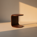 Round walnut C-shaped side table in a plaster room at golden hour