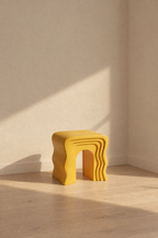 Yellow sculptural wave stool in a quiet room corner